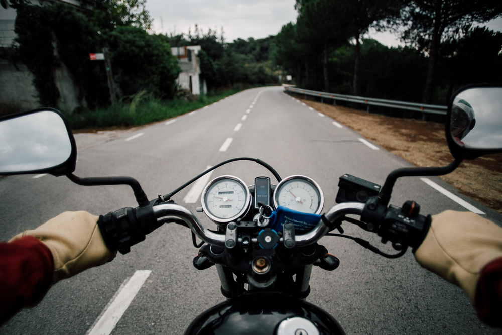 An Introduction to Motorcycle Safety - POV from drivers point of view of motorcycle handlebar with speedometer and rear view windows, driving on quiet empty mountain road, driver wears leather gloves and steers confidently
